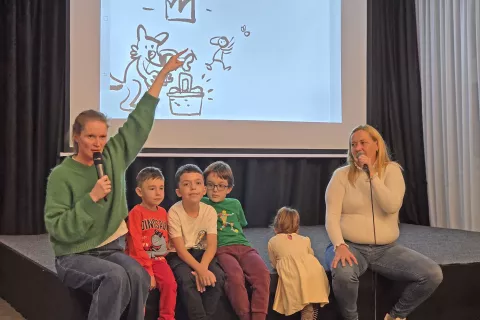 Pripovedovalka &Scaron;pela Frlic, prevajalka Vesna Berisha in poslu&scaron;alci, v ozadju so sproti nastajale podobe izpod rok ilustratorja Mihe Hančiča. / Foto: &Scaron;pela &Scaron;imenc