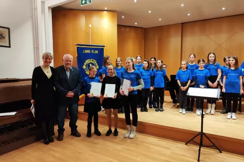 Barbara Božič in predsednik Matevž Bergant iz Lions kluba Kamnik ter tri obetavne učenke Glasbene &scaron;ole Kamnik, vsaka s posebnim priznanjem in knjižno nagrado: Anamarija Graj, Tina Bizjak in Tamara Kralj (od leve proti desni). V ozadju članice Mladinskega pevskega zbora G&Scaron; Kamnik. / Foto: Katja Dolenc