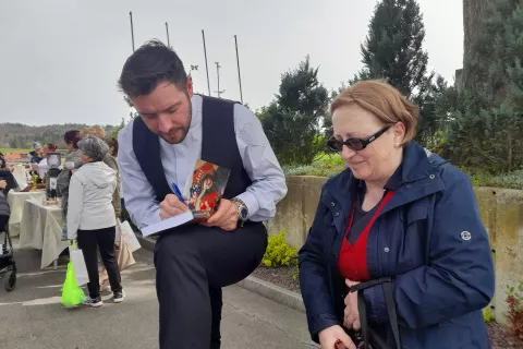 Župnik Martin Golob preprosto, kar na kolenu, podpisuje svojo knjigo. / Foto: Jože Ko&scaron;njek