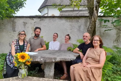 Predsednica Slovenskega prosvetnega društva Kočna iz Sveč (levo) z umetniki za kamnito mizo na vrtu Goršetove galerije. / Foto: Jože Košnjek