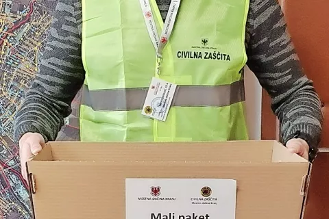 Prostovoljec s kranjske občine z identifikacijsko kartico okrog vratu in malim paketom hrane v rokah / Foto: MO Kranj / Foto: 