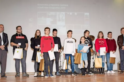 Med Izidorjem Jesenkom, predsednikom FD Anton Ažbe, in Igorjem Debevcem, predsednikom Fotografske zveze Slovenije, so se na odru predstavili nagrajeni mladi fotografi. / Foto: Branko Košir / Foto: 